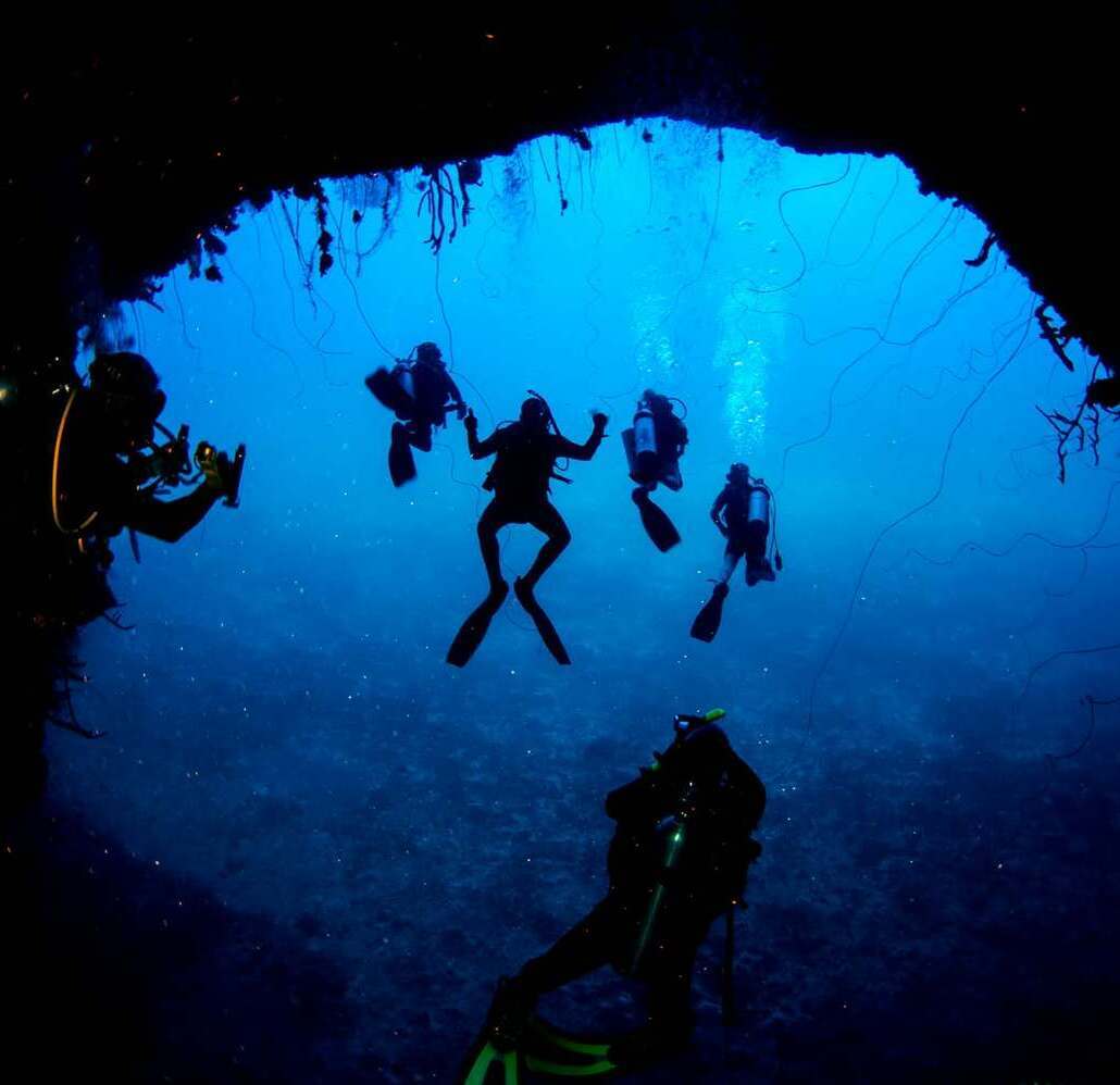 Group of scuba divers silhouetted inside a cavern at Cabo Cabrón National Park